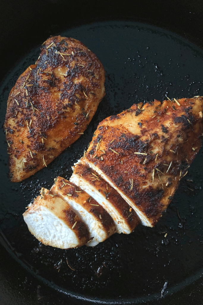 two chicken breasts in a cast iron pan, one breast is sliced
