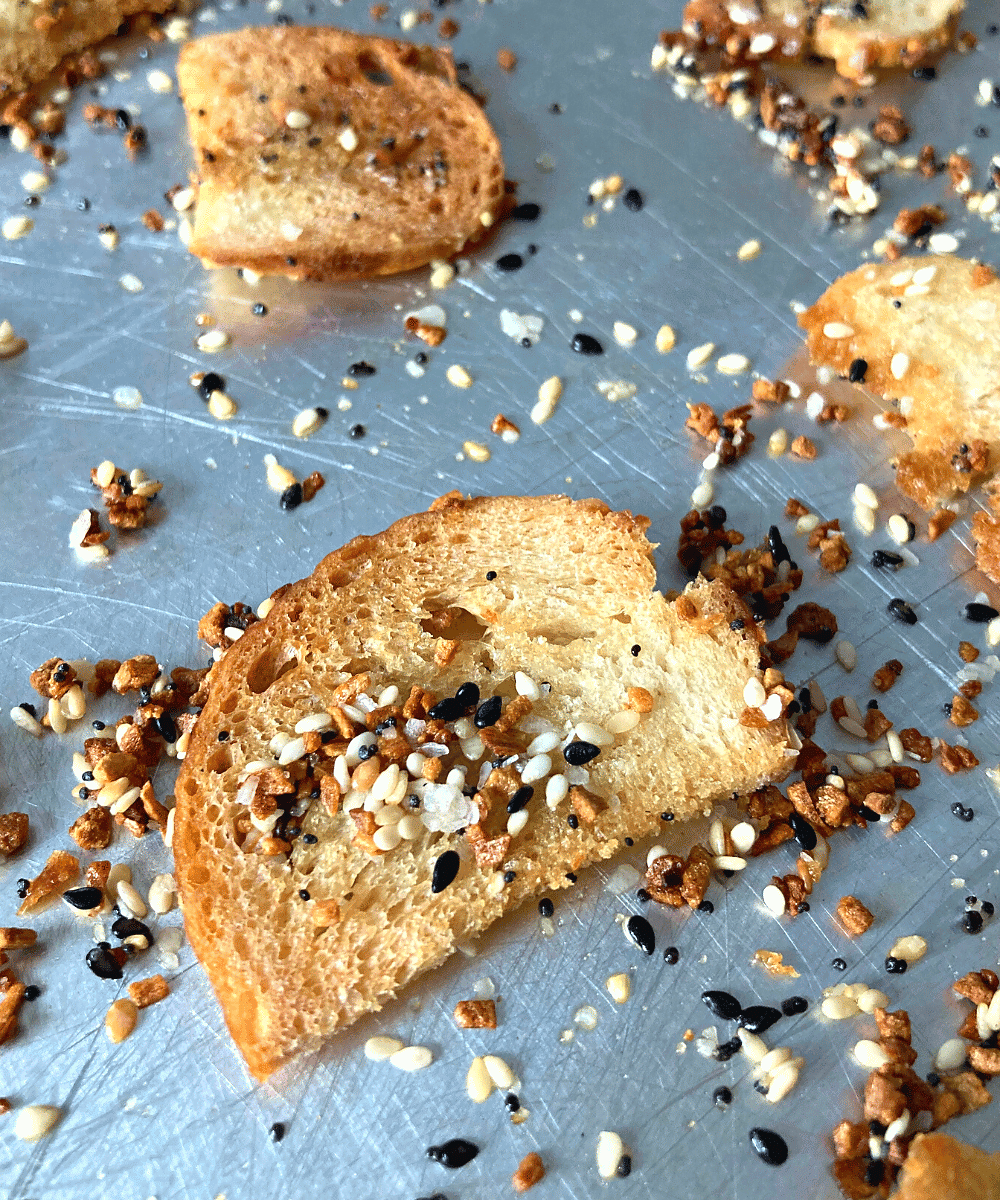 sourdough bagel chips on a baking sheet with everything but the bagel seasoning