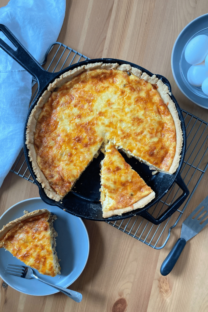 cast iron skillet quiche sliced in two pieces, one in the cast iron skillet and the other on a plate