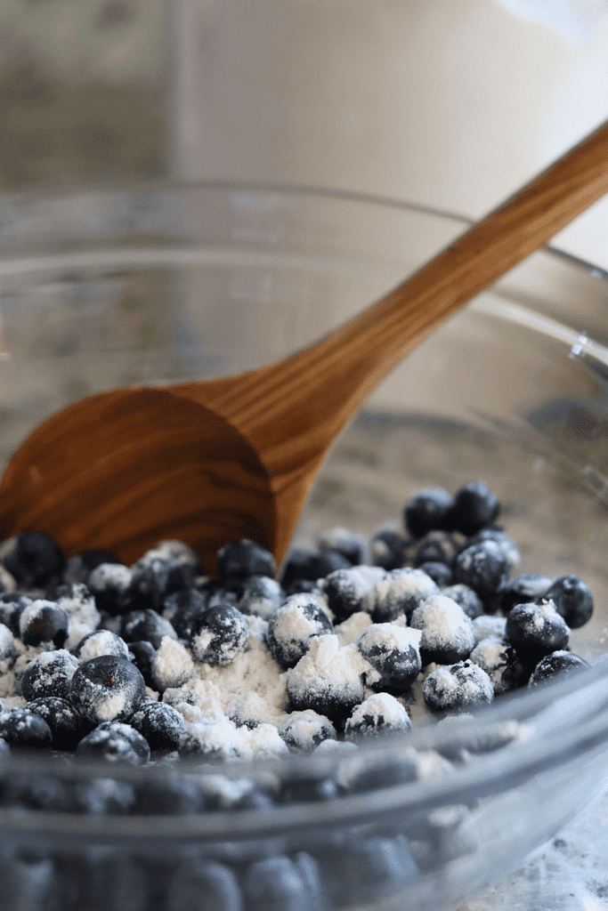 Flour on fresh blueberries and a wooden spoon