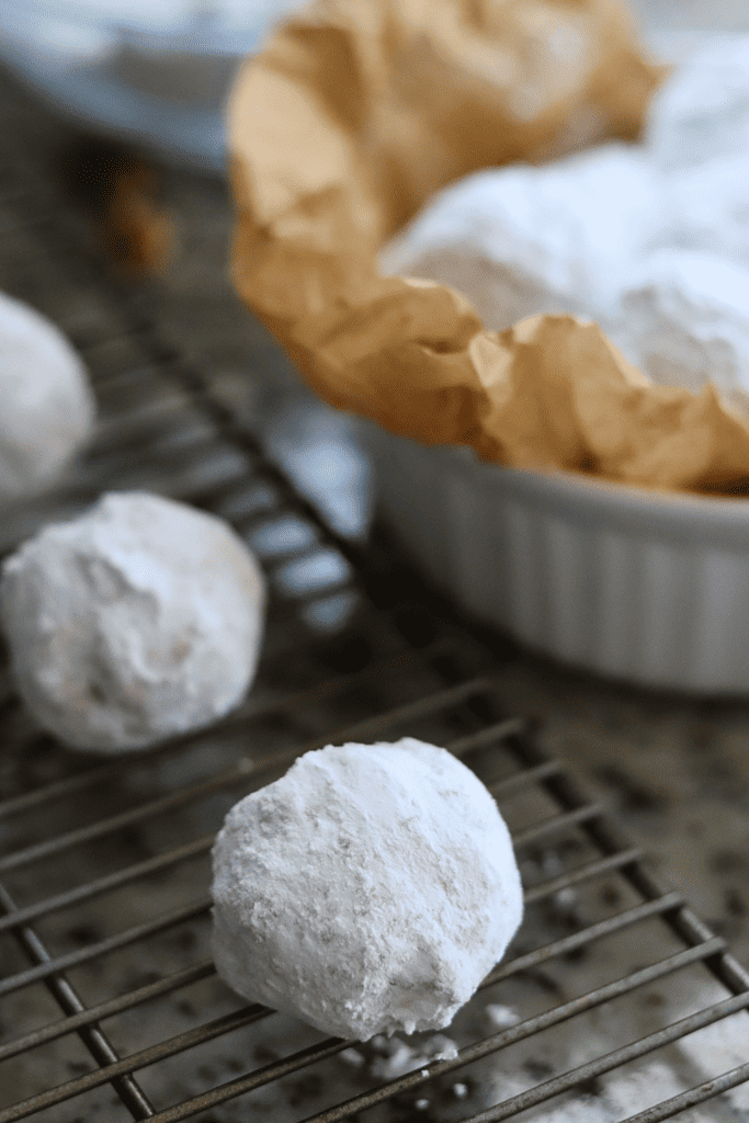 sourdough snowball cookies on a wire rack and in a bowl with parchment paper