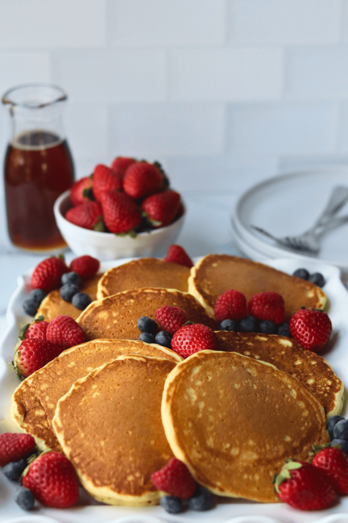 pancakes with blueberries and strawberries arranged nicely on a white plate