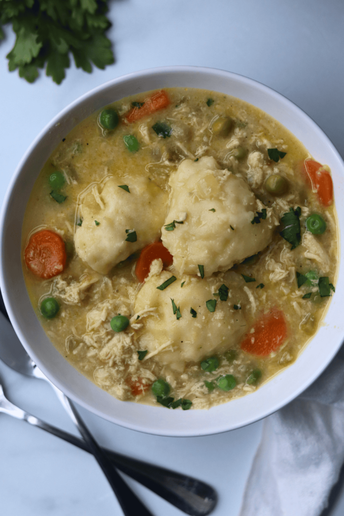 chicken and dumpling soup in a white bowl with utensils on the side