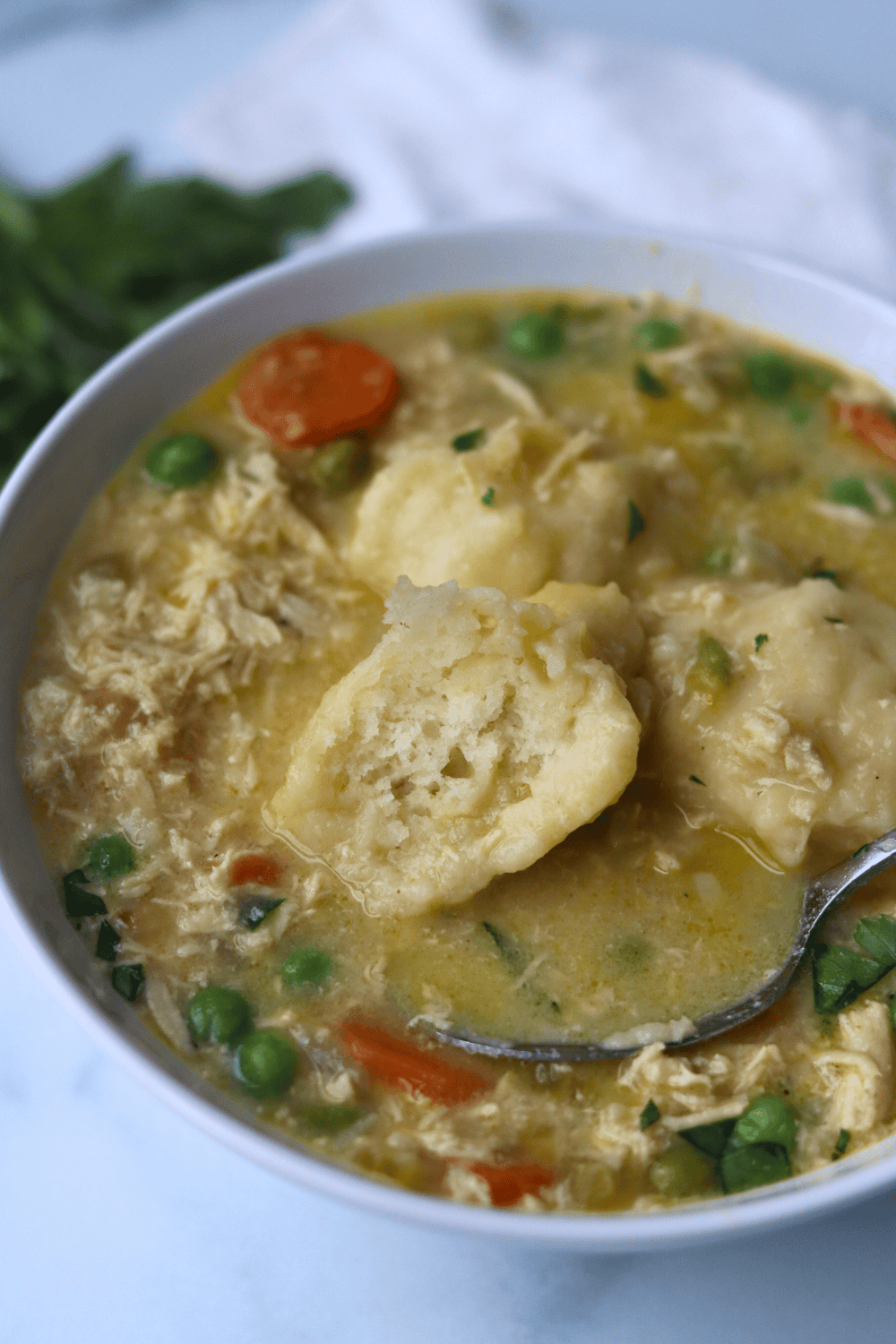 chicken and dumpling soup in a white bowl with spoon.