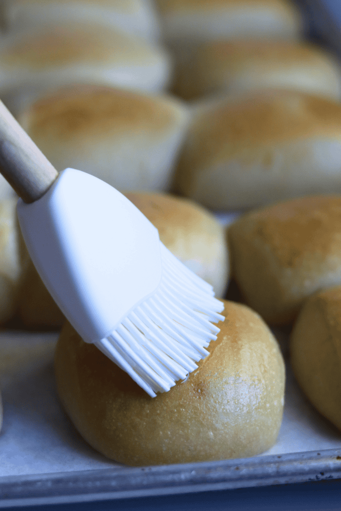 brushing butter on top of baked sourdough texas roadhouse dinner rolls